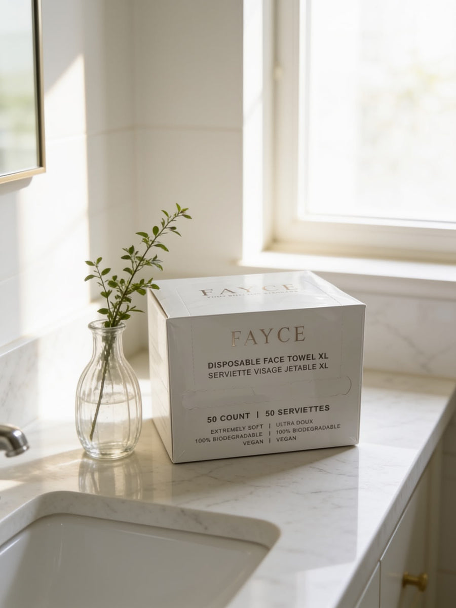 FAYCE Disposable Face Towel XL box, 50 count, on a marble vanity beside a glass vase in a sunlit bathroom
